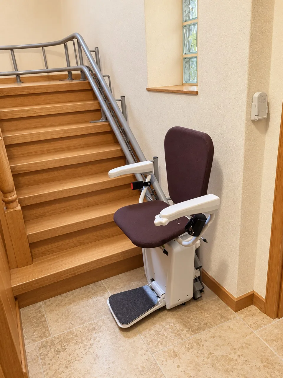 Sitzlift mit dunklem Sitz, Armlehnen und Fußplatte am unteren Ende einer Holztreppe.